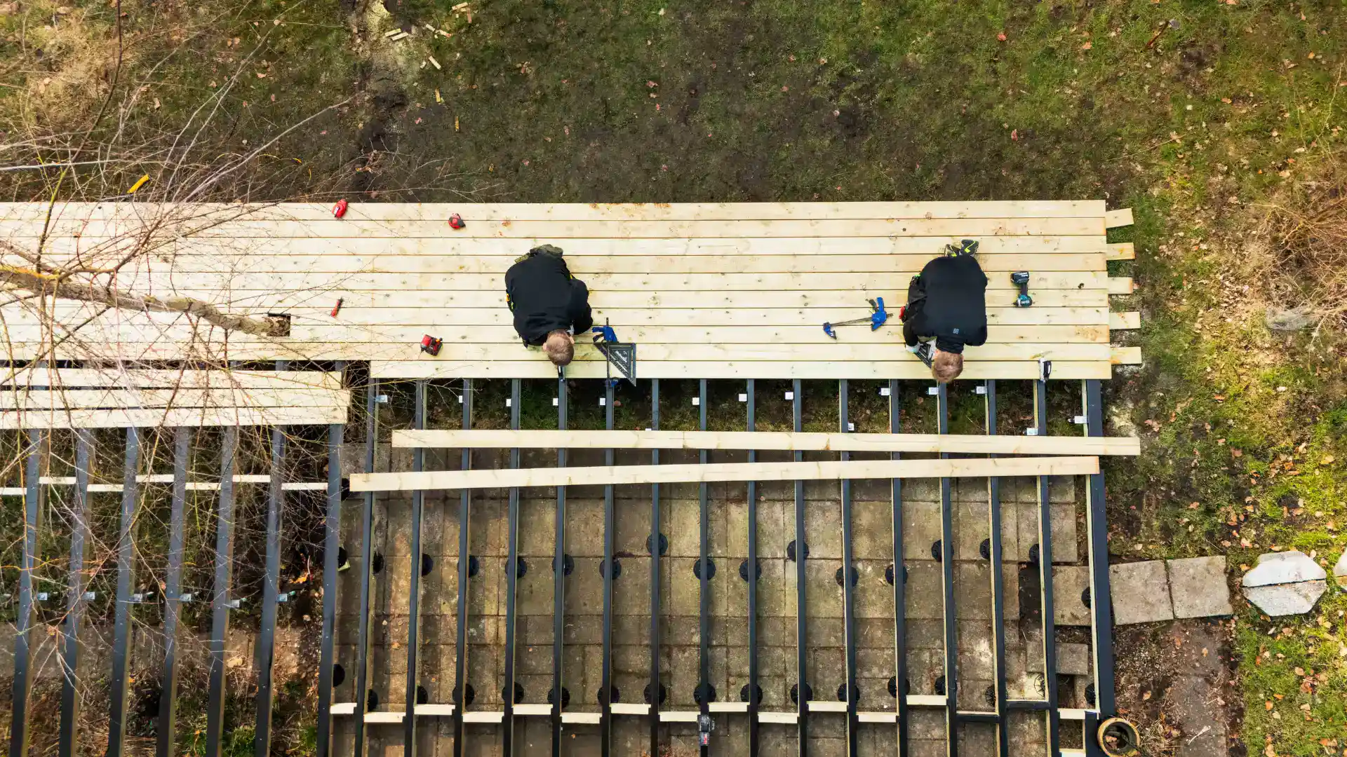 Arbejdere bygger træterrasse med træplanker og værktøj.