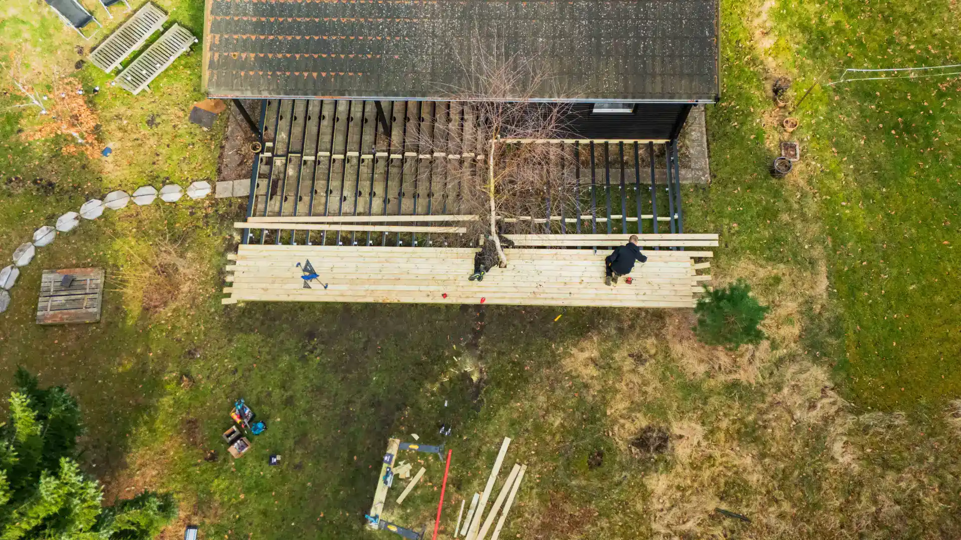 Billedet viser en person, der arbejder på en træterrasse foran en bolig.